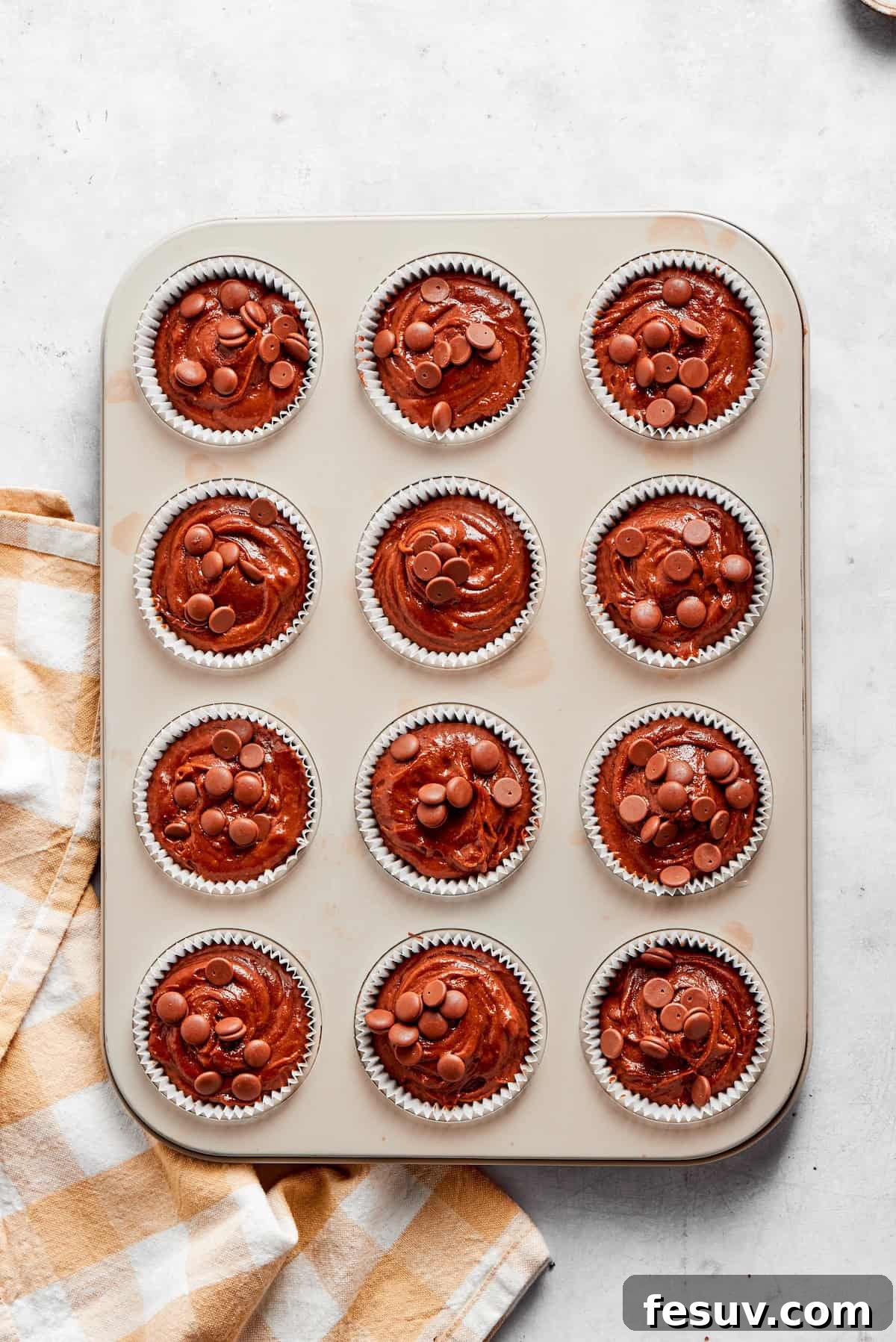 Rich chocolate muffin batter is neatly divided into individual muffin cups within a lined muffin tin, ready for baking.