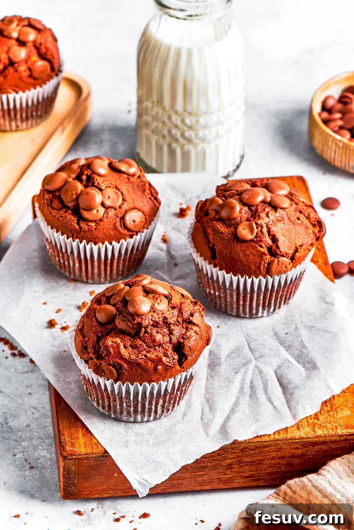 Three perfectly baked chocolate muffins presented on a wooden board, with a glass of milk in the background, inviting a delicious snack or breakfast.