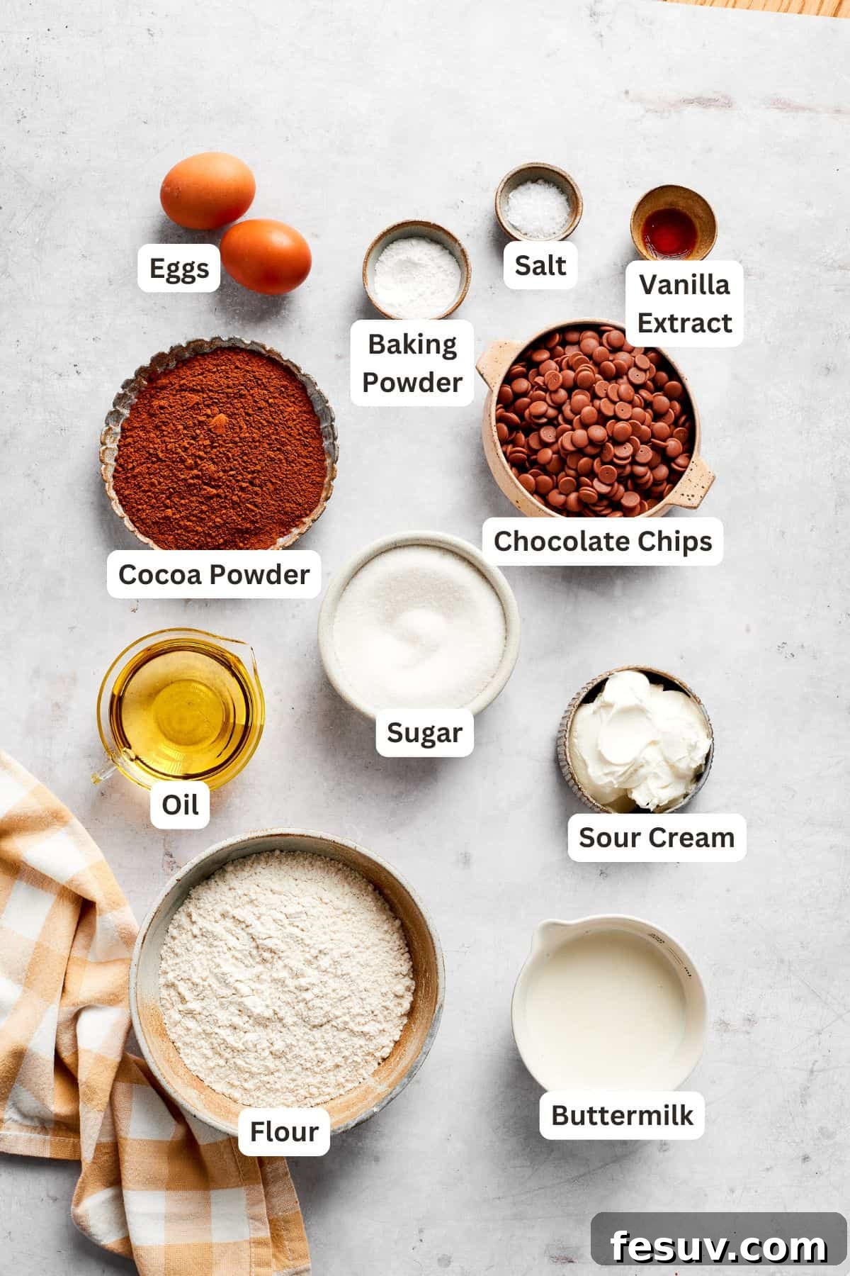Carefully arranged ingredients for chocolate muffins, clearly labeled for easy identification, on a rustic wooden surface.