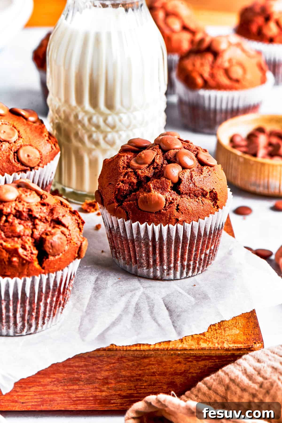 A delightful presentation of chocolate muffins on a rustic wooden board, with a refreshing glass of milk in the soft-focus background, inviting enjoyment.
