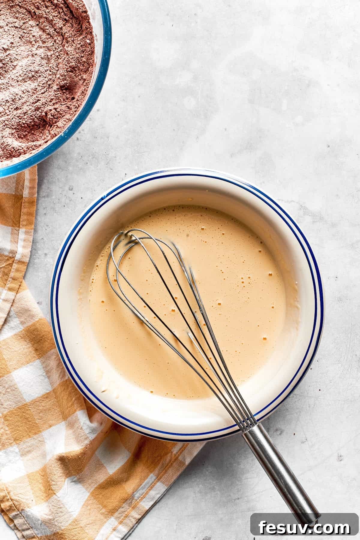 The wet mixture for chocolate muffins, a blend of eggs, sour cream, oil, buttermilk, and vanilla, is smoothly whisked in a bowl.