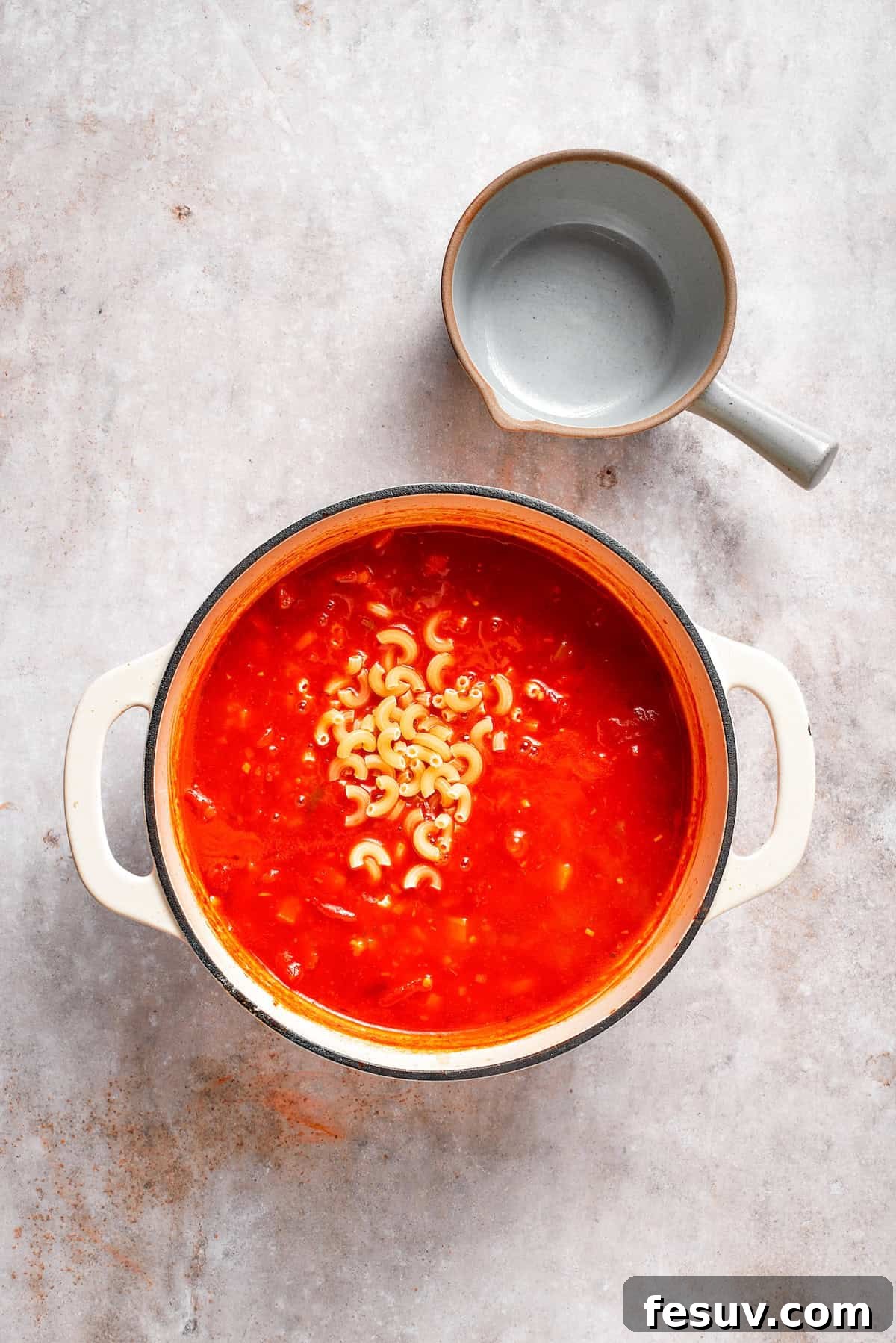 Elbow macaroni being stirred into the simmering tomato Florentine soup in a pot.