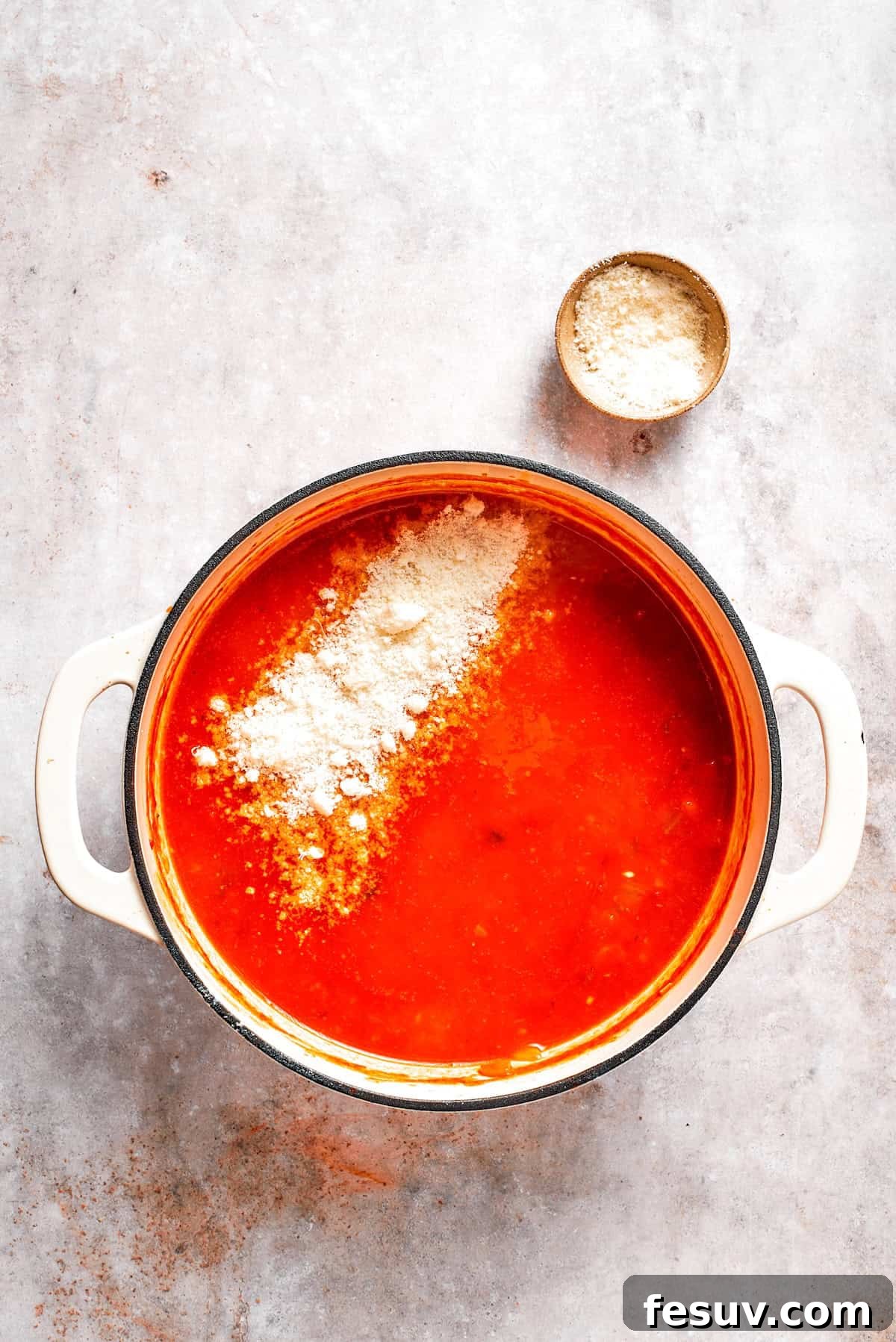 Grated Parmesan cheese being stirred into the hot Tomato Florentine soup in a pot, melting into a creamy consistency.