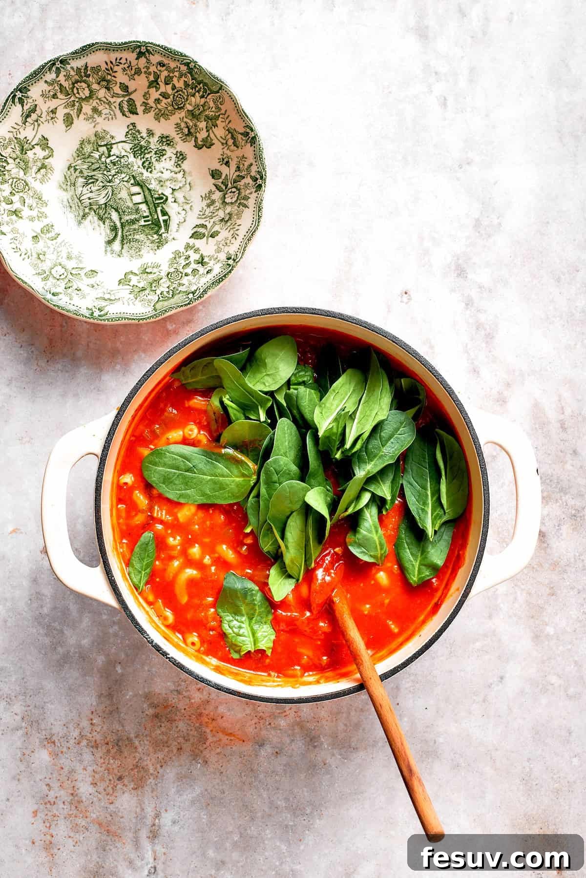 Fresh baby spinach leaves being gently folded into the hot Tomato Florentine soup, wilting beautifully.