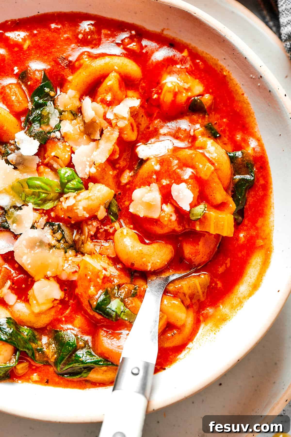A spoon stirring through a bowl of steaming Tomato Florentine soup, highlighting the tender spinach and macaroni pasta amidst the rich tomato broth.