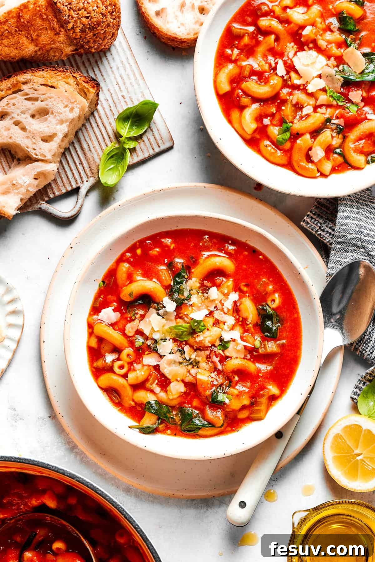 Two bowls of steaming Tomato Florentine soup, garnished with fresh basil and Parmesan, with crusty bread and spoons beside them on a wooden surface.