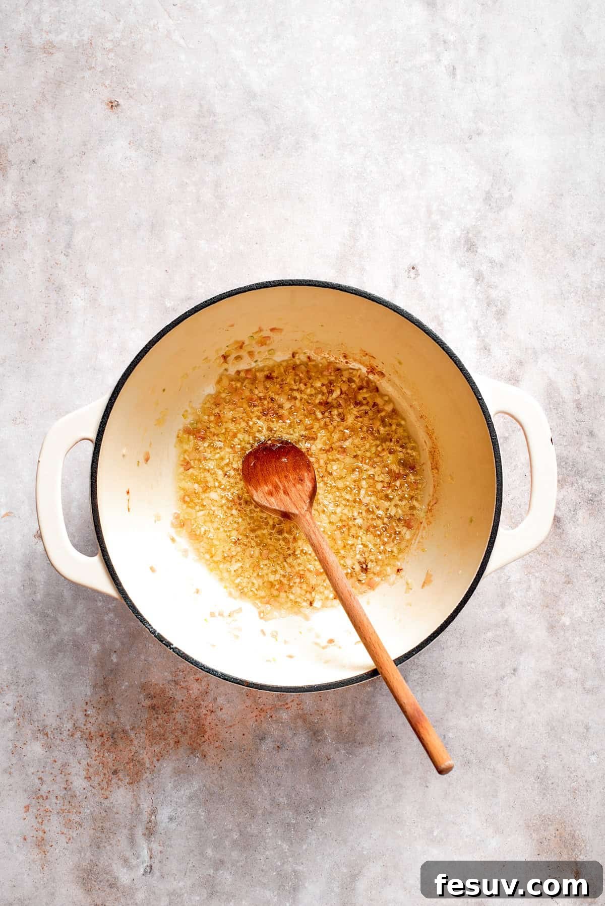 Minced garlic being added to sautéed shallots in a soup pot, releasing its fragrant aroma.