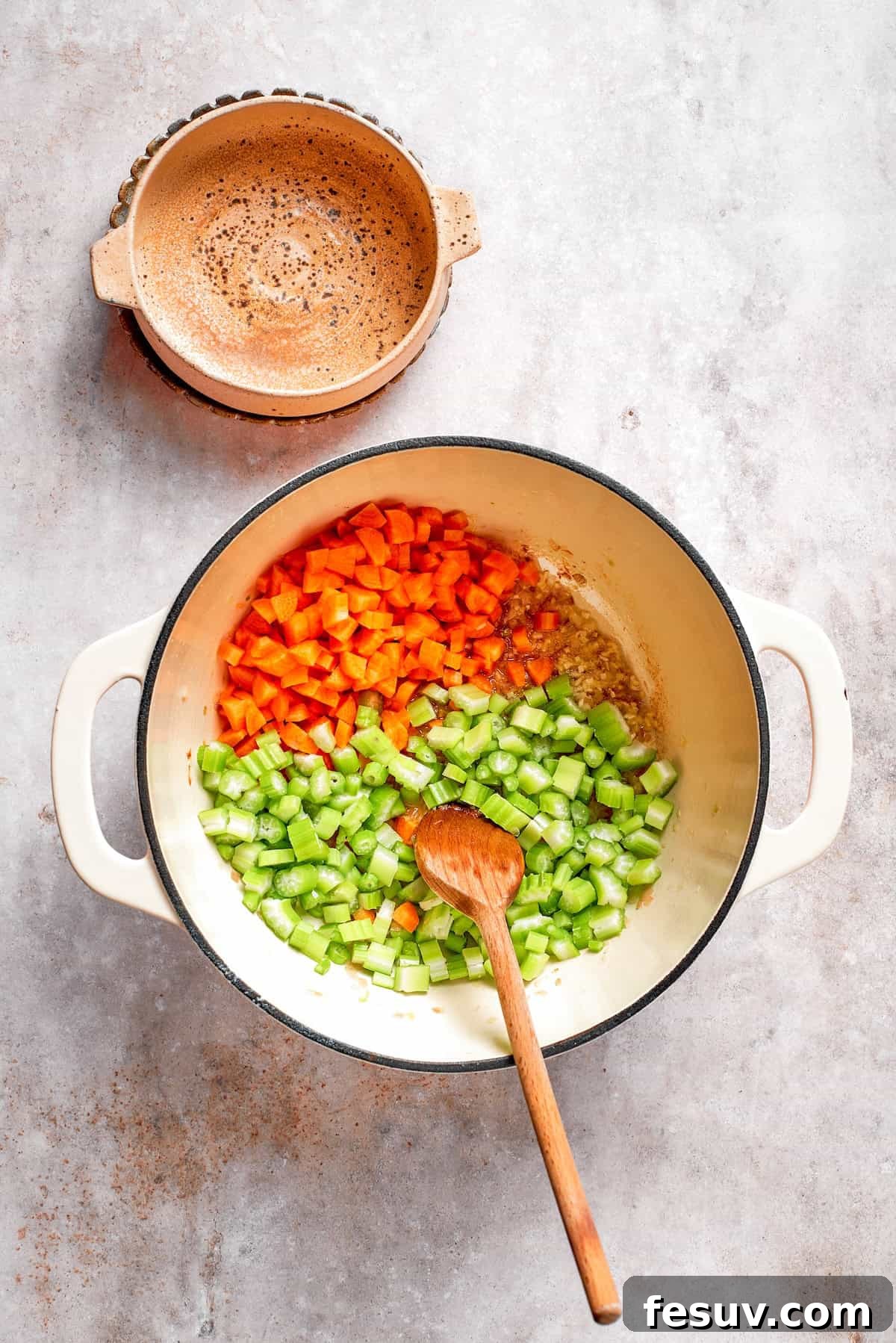 Chopped celery and carrots being added to the sautéed shallots and garlic in a soup pot.