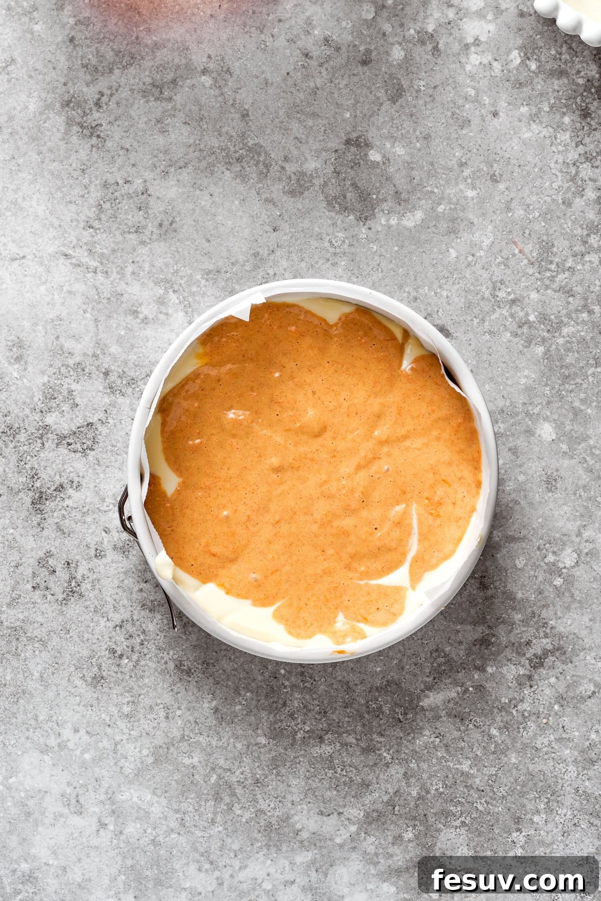A layer of carrot cake is placed in a cake pan.