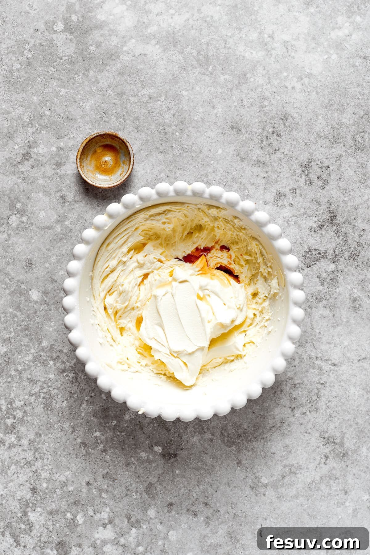 Vanilla is added to a bowl of cream cheese frosting.