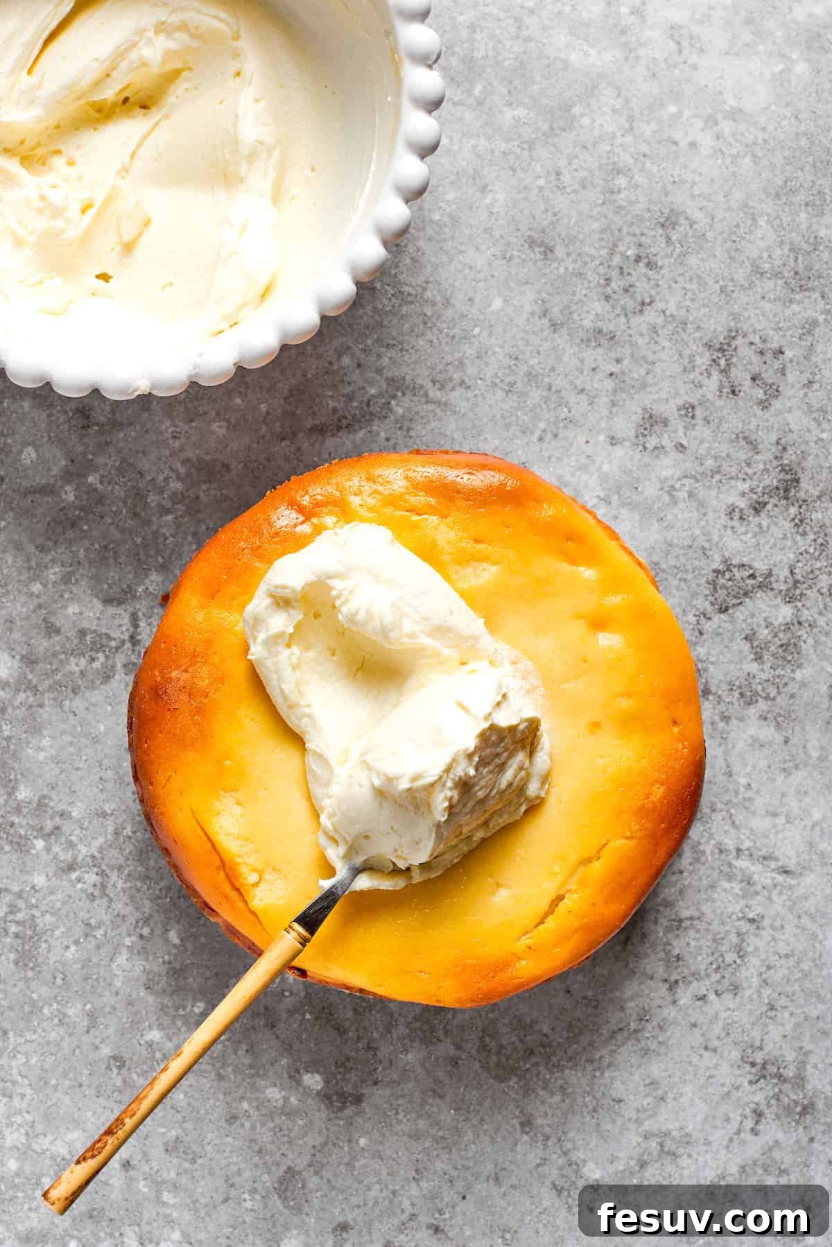 Cream cheese frosting is spread on the top of a carrot cake cheesecake,