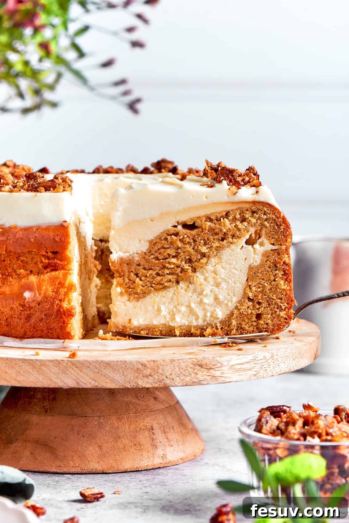 A slice is removed from a platter of carrot cake cheesecake, showing the distinct layers.