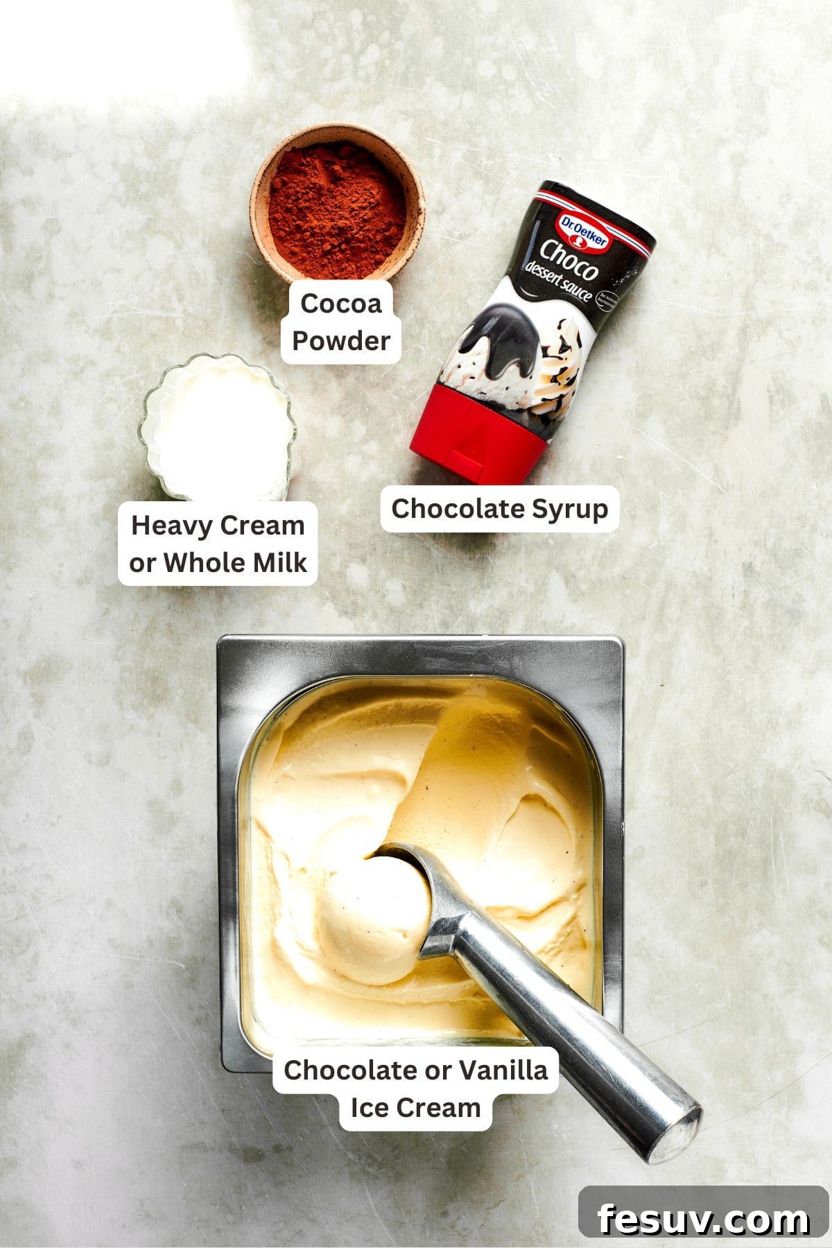 Labeled ingredients for a chocolate milkshake, including vanilla ice cream, heavy cream, cocoa powder, and hot fudge sauce, neatly arranged on a counter.