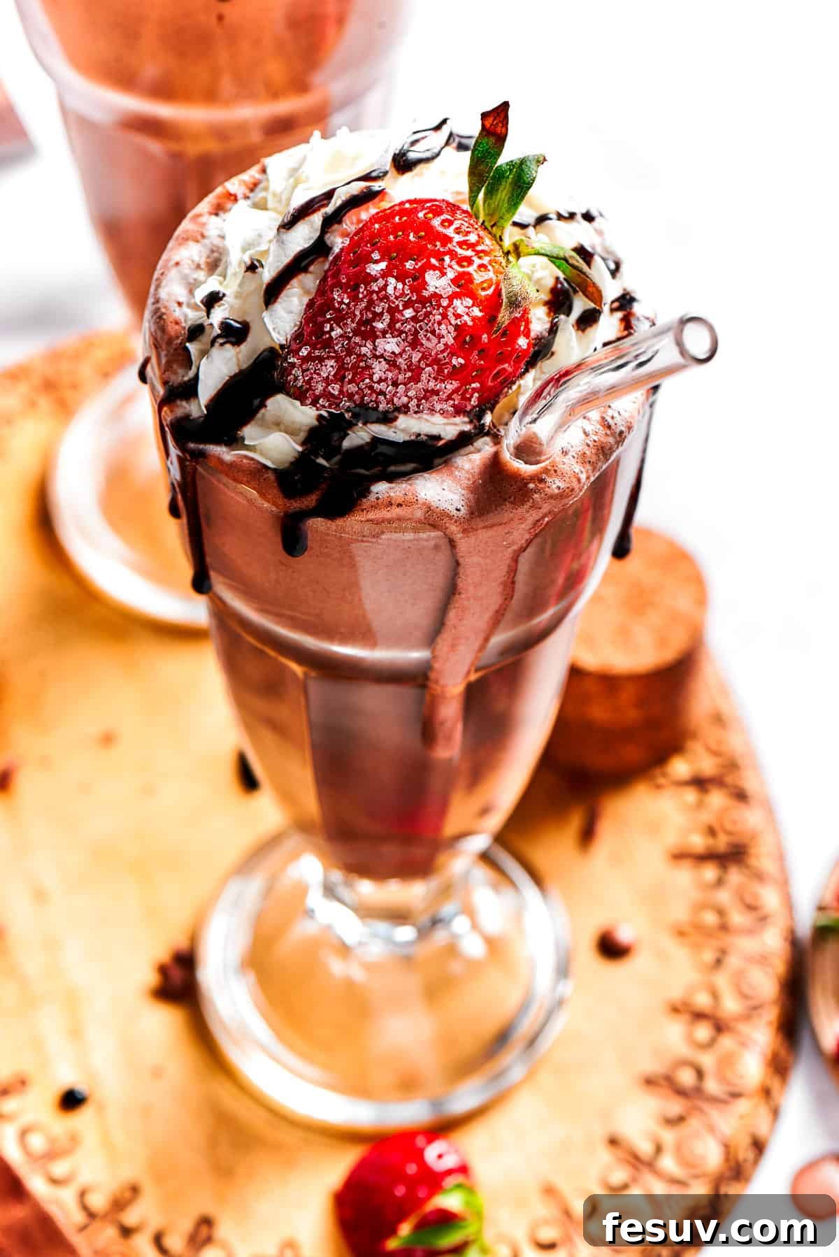 A tall glass filled with a creamy chocolate milkshake, elegantly garnished with a generous swirl of whipped cream, a fan of fresh strawberries, and a delicate chocolate drizzle.