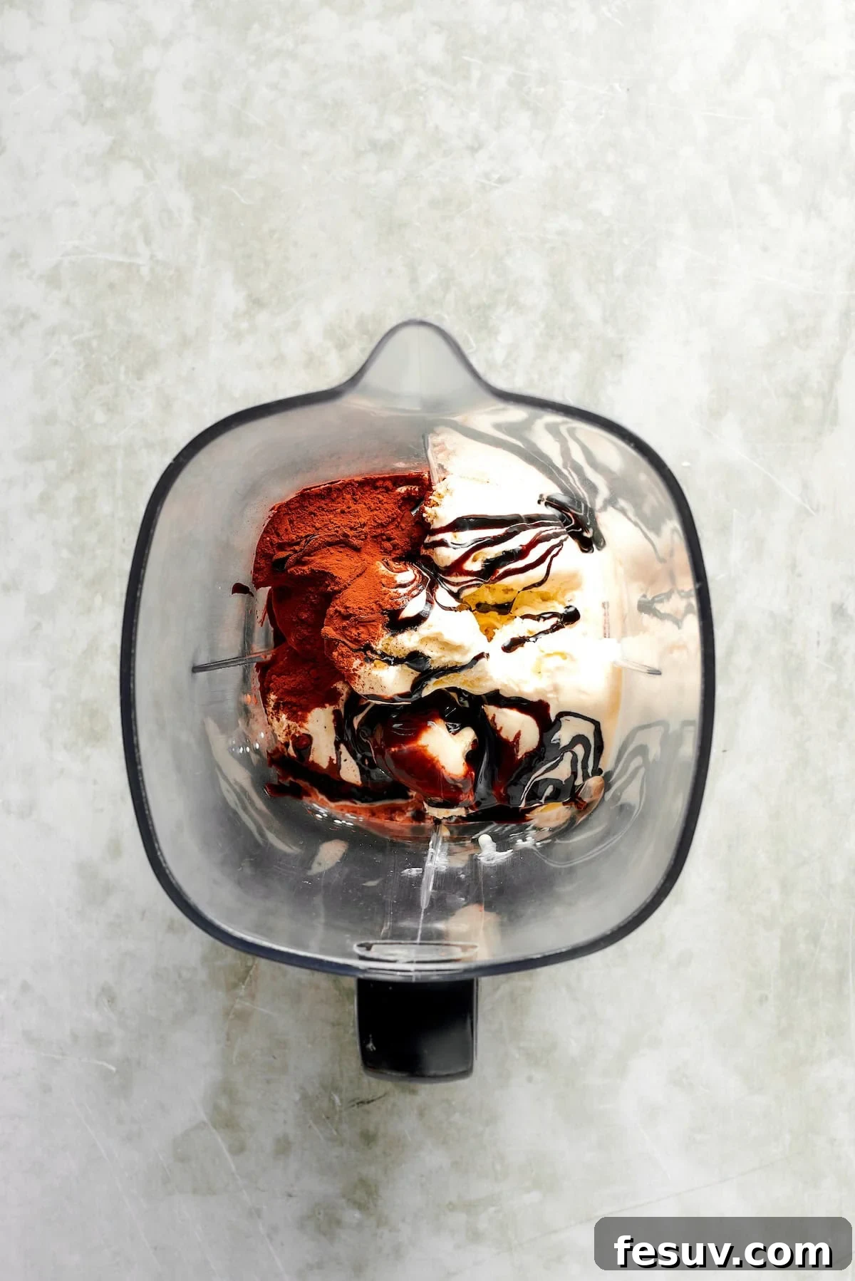 Ingredients for chocolate milkshakes are carefully added to a high-powered blender, showing ice cream, cocoa, and liquid.