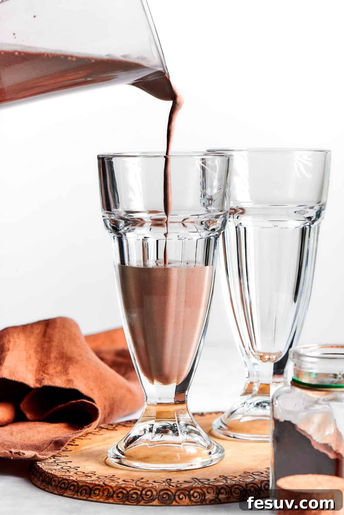 A stream of rich, thick chocolate milkshake is poured from a blender into a tall, chilled glass.