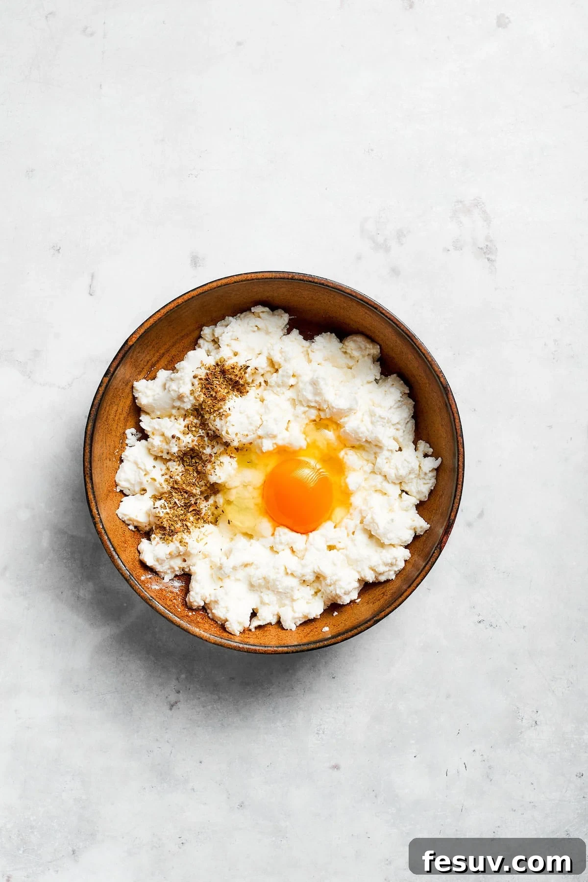 An egg is added to ricotta cheese in a bowl for the creamy filling.