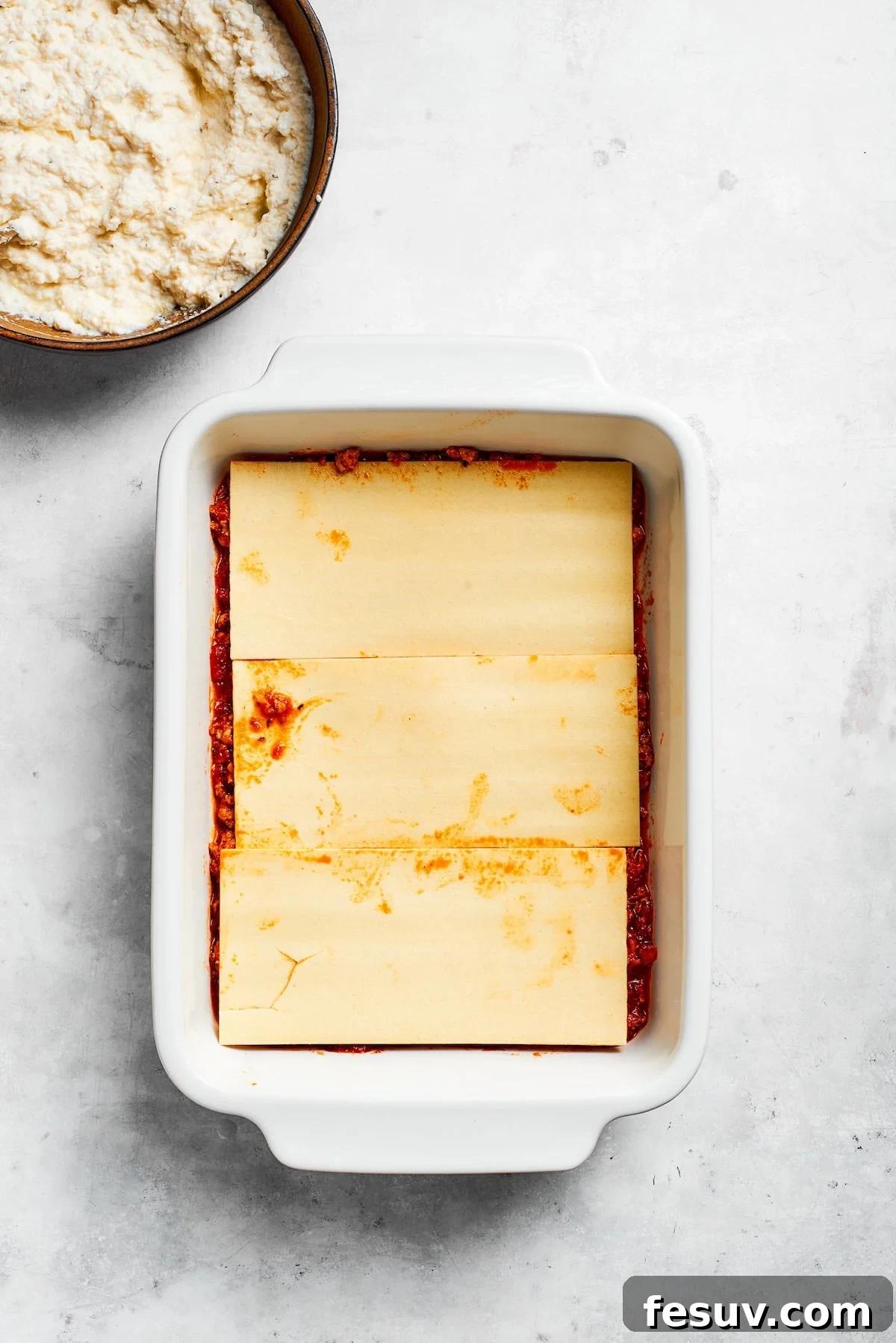 Lasagna sheets are carefully layered in a baking pan, forming the base.