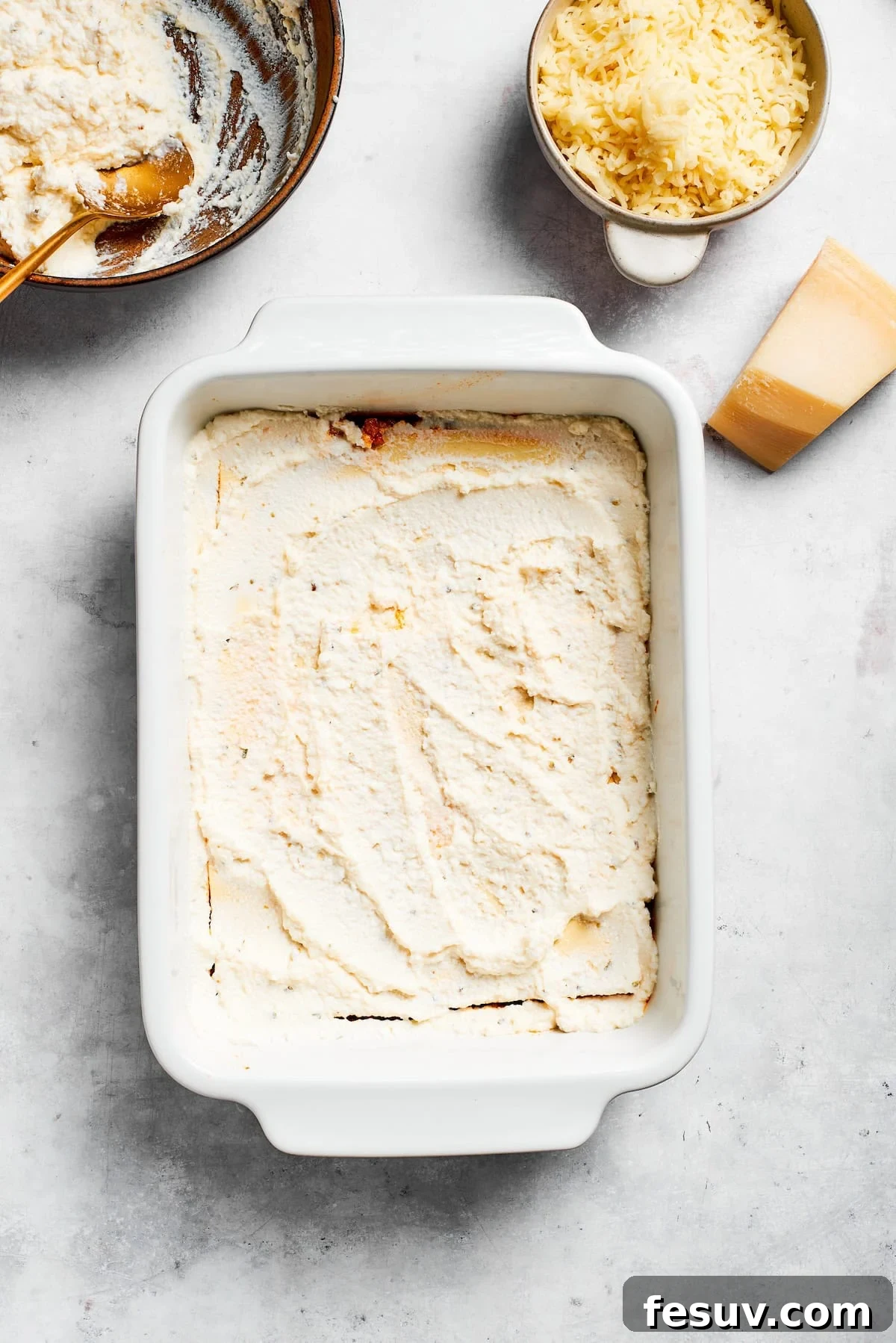 Ricotta cheese is spread evenly over a layer of pasta for lasagna.