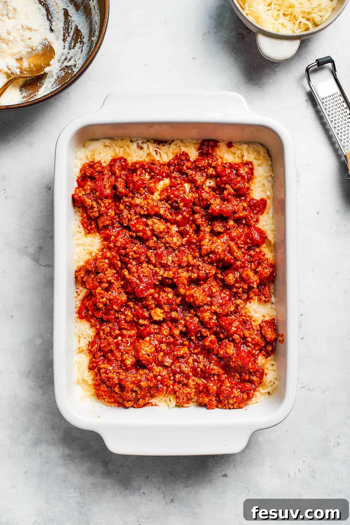 Meat sauce is added to beef lasagna layers, preparing for the next set of noodles.