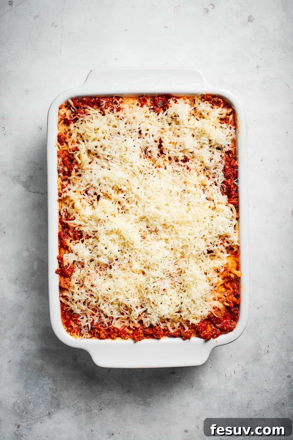 A final layer of cheese on top of a pan of beef lasagna, ready for baking.