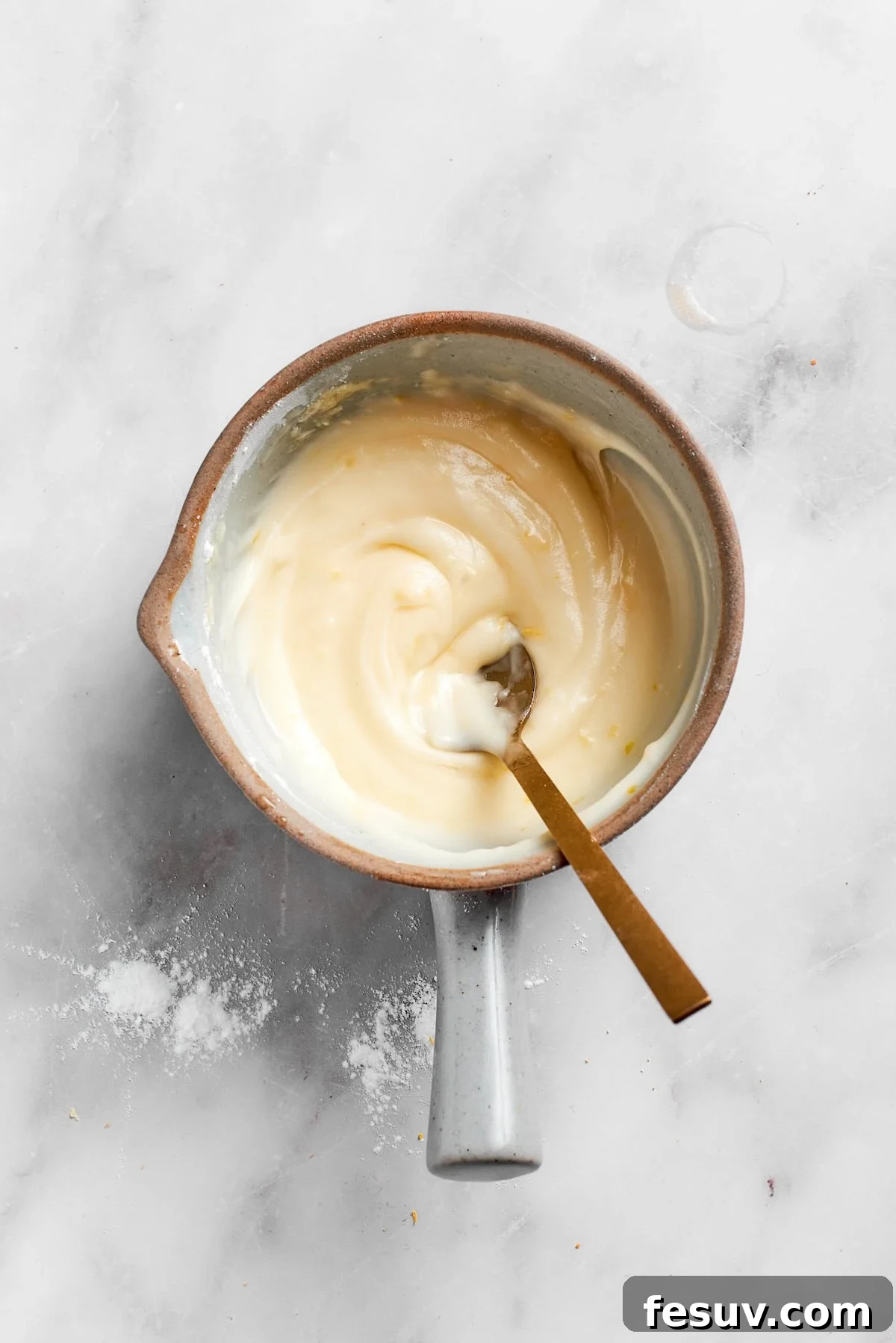 A spoon stirring the lemon frosting in a pot, showing its thick yet spreadable consistency.