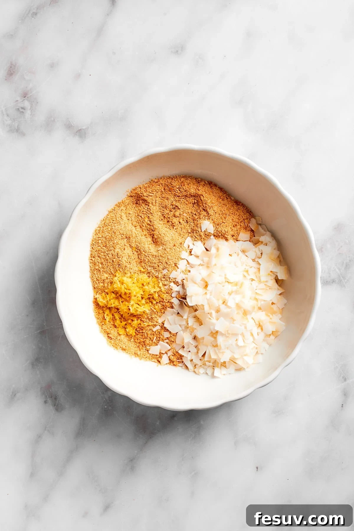 Sweetened flaked coconut being added to a bowl of crushed graham cracker crumbs.