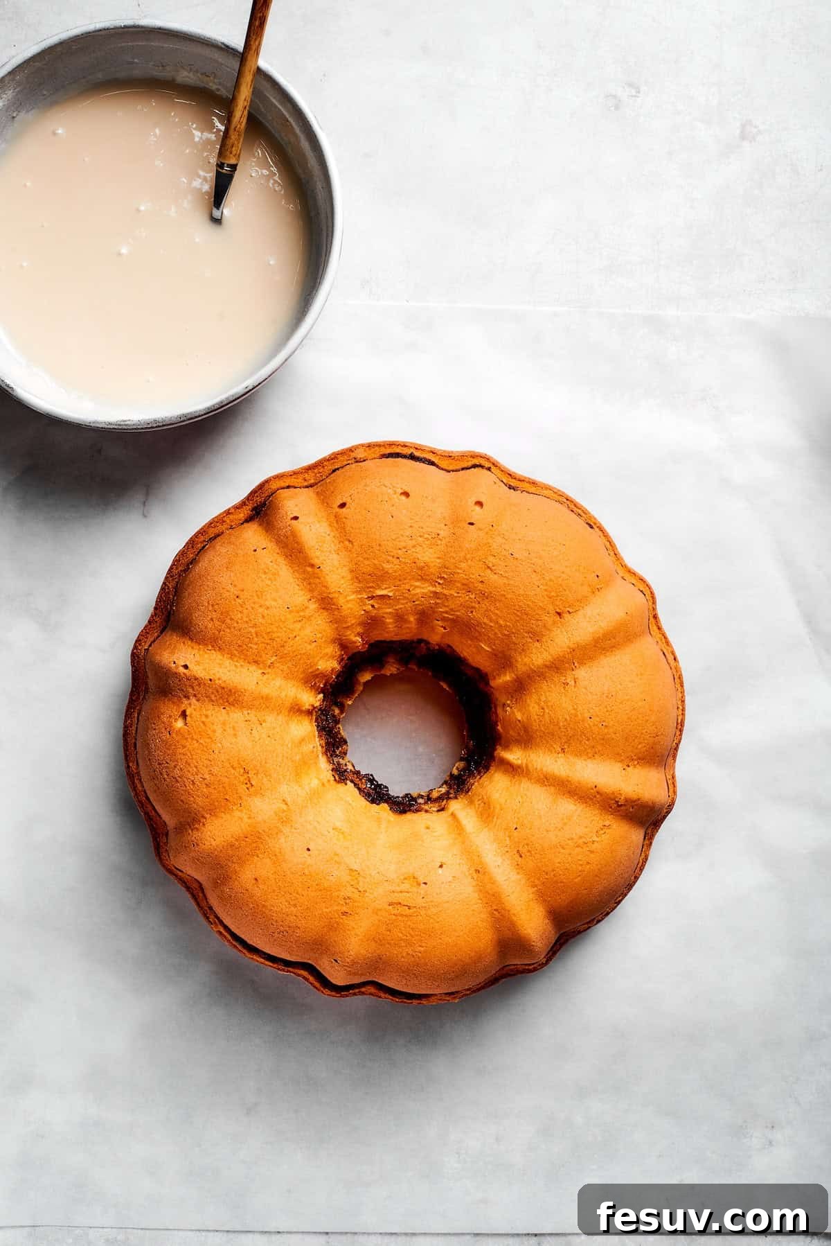 The 'Just One More' Cake 16 A freshly baked Bundt cake cooling on a wire rack beside a bowl of prepared icing.