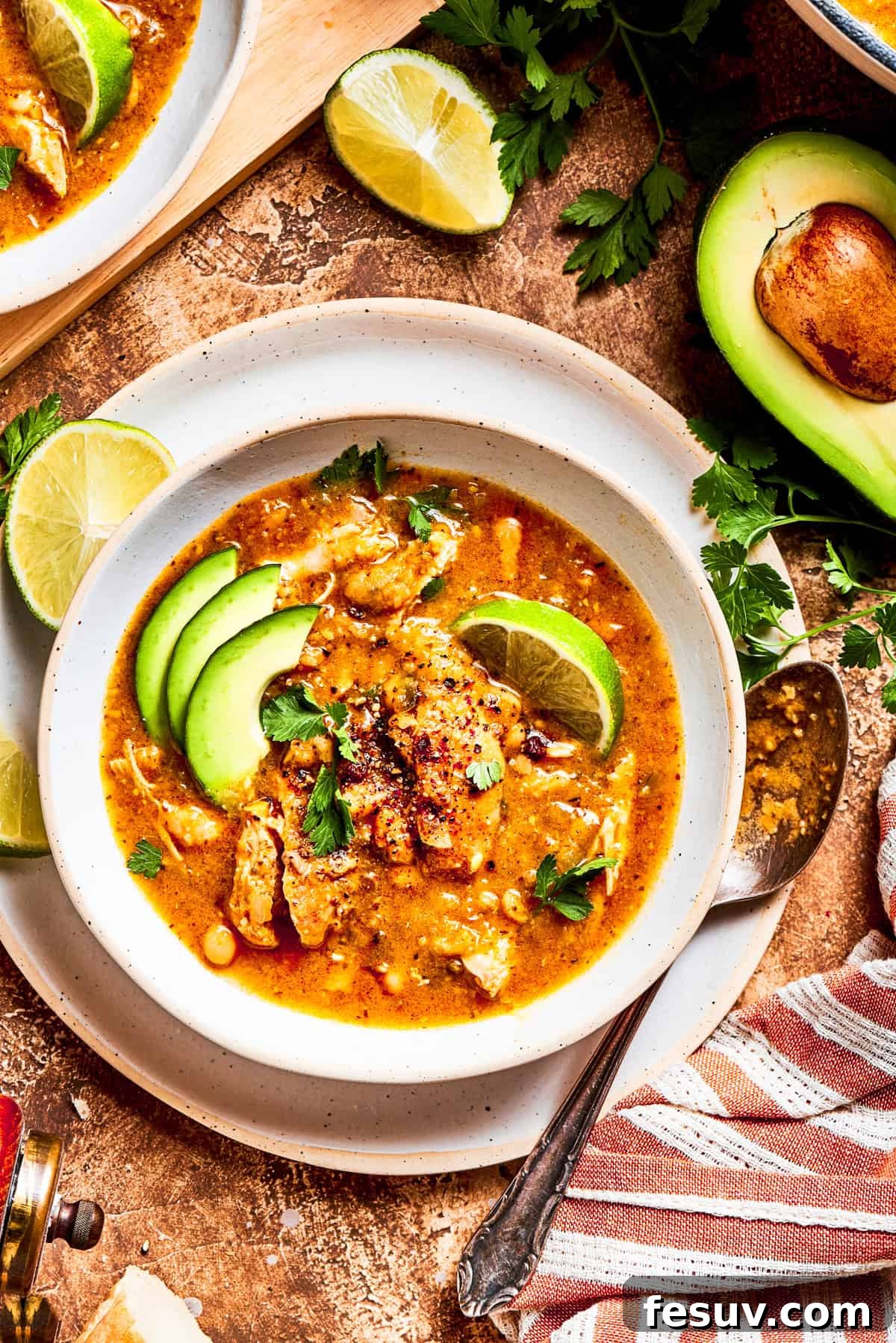 Tender chicken and pinto beans are cooked in a zesty broth made with salsa verde and green chilis to make spicy chicken soup. Spicy chicken soup in a bowl garnished with avocado slices and lemon wedges.