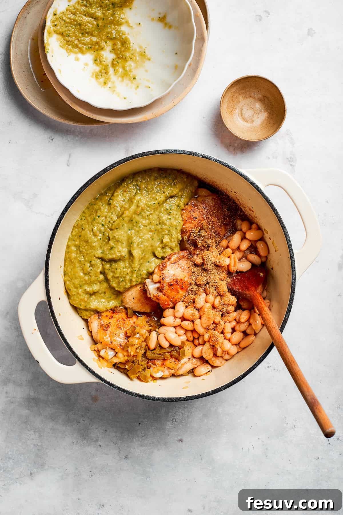 Tender chicken and pinto beans are cooked in a zesty broth made with salsa verde and green chilis to make spicy chicken soup. Ingredients for spicy chicken soup are added to a soup pot.