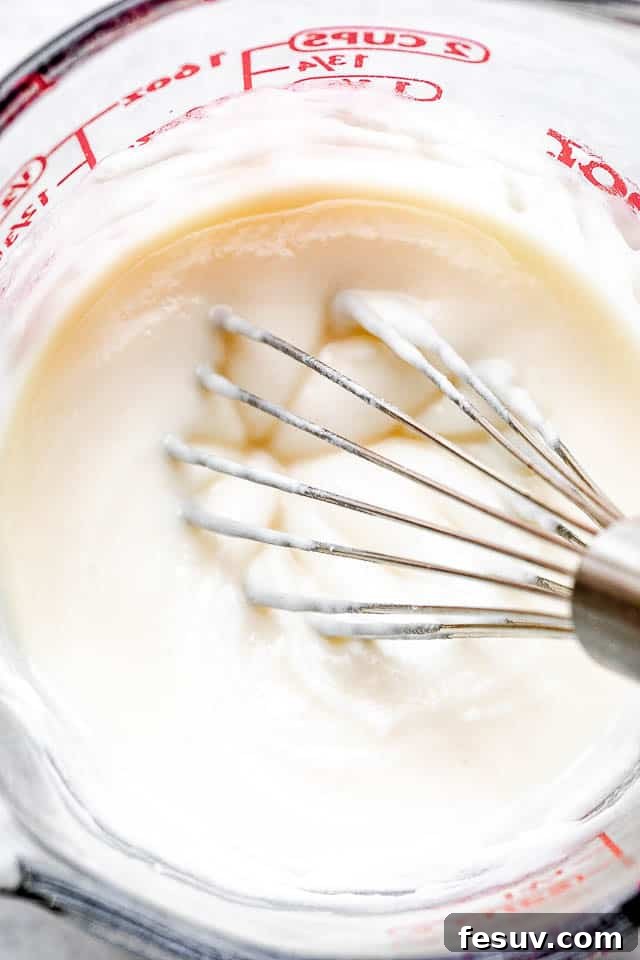 whisking cream cheese frosting in a glass measuring cup