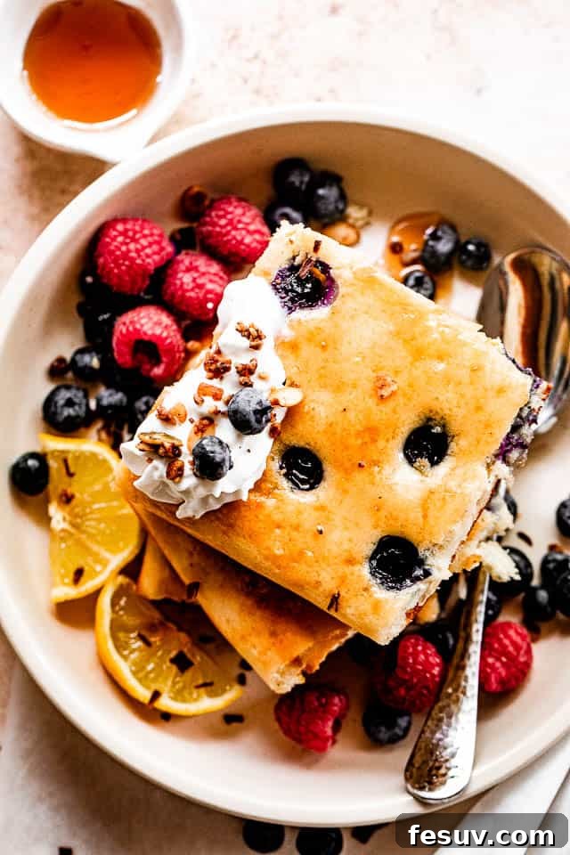 Effortless Sheet Pan Pancakes 5 top shot of squared pancakes topped with whipped cream, berries around the pancakes, and maple syrup to the side