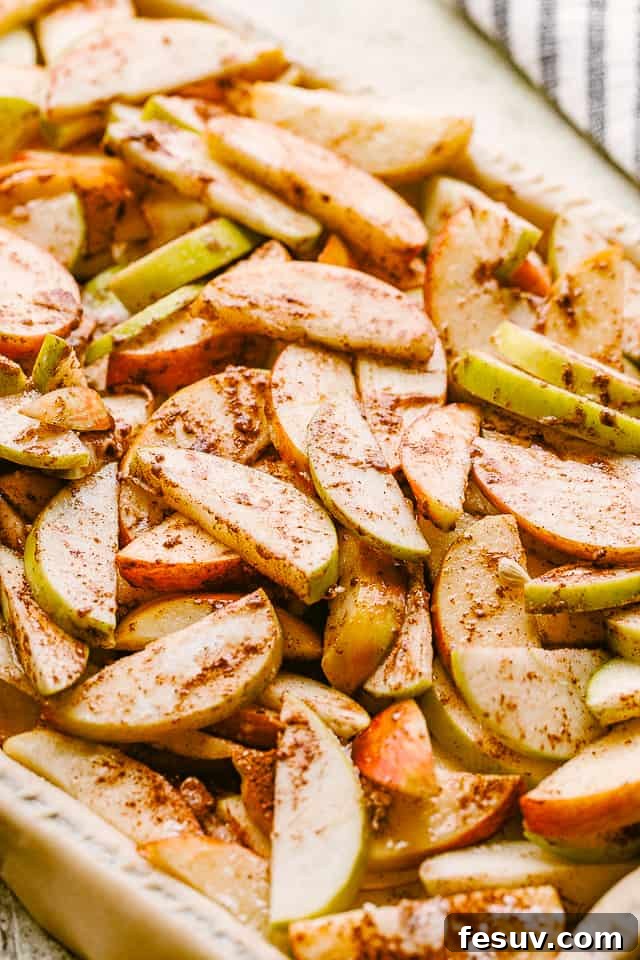 Thinly sliced apples, vibrant and fresh, generously tossed with sugar and cinnamon in a large bowl.