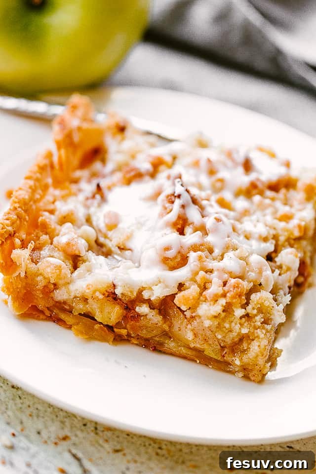 A perfectly sliced piece of Dutch apple slab pie presented on a white dessert plate, with a fresh green apple nearby for garnish.