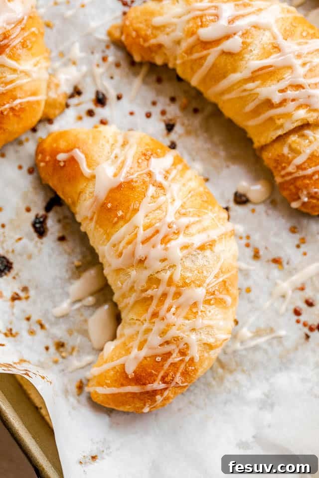 These Pumpkin Crescent Rolls are the best fall treat! Buttery rolls stuffed with a sweet pumpkin cream cheese filling and drizzled with vanilla glaze. Top shot of glazed pumpkin cheesecake crescent rolls, highlighting their golden-brown perfection and sweet drizzle.