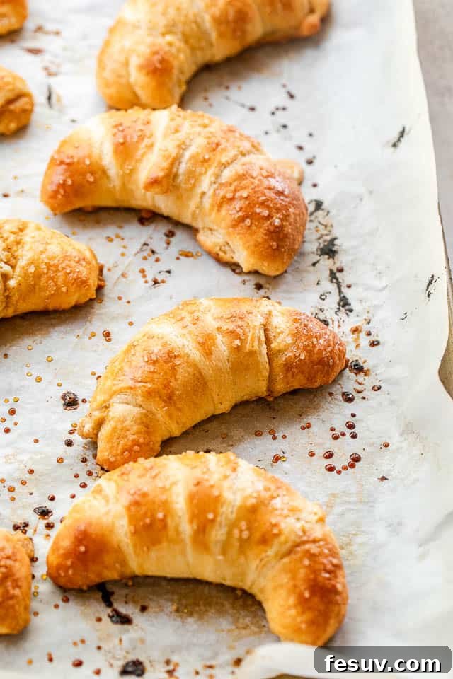 These Pumpkin Crescent Rolls are the best fall treat! Buttery rolls stuffed with a sweet pumpkin cream cheese filling and drizzled with vanilla glaze. Side shot of a baking sheet filled with freshly baked pumpkin crescent rolls, cooling on a wire rack.