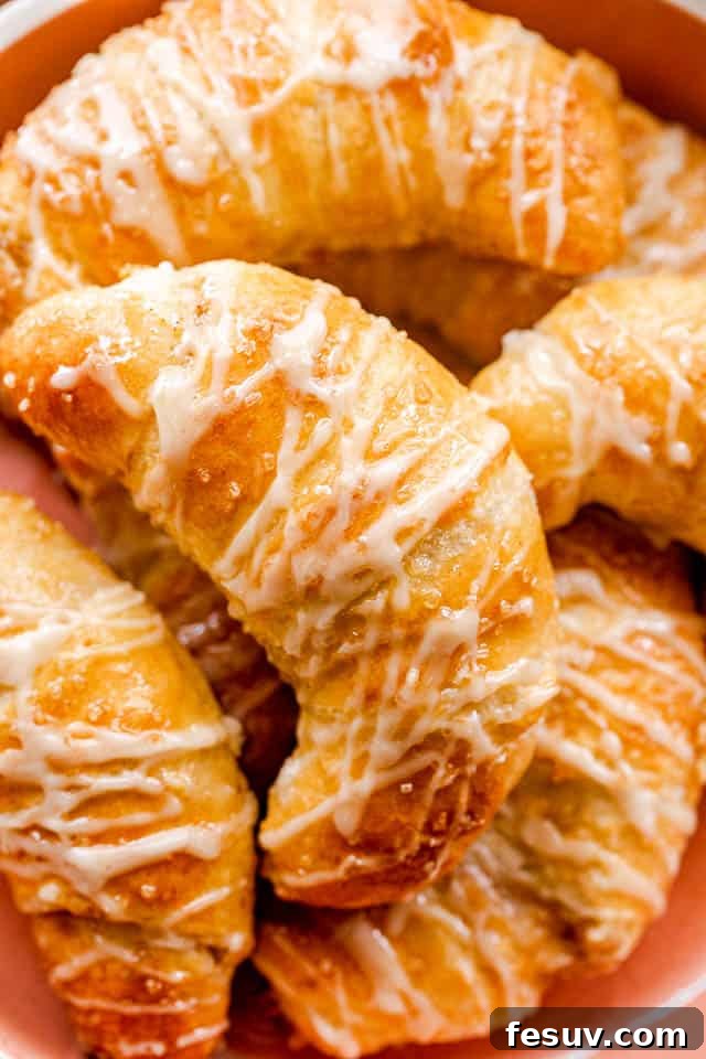 These Pumpkin Crescent Rolls are the best fall treat! Buttery rolls stuffed with a sweet pumpkin cream cheese filling and drizzled with vanilla glaze. Prepared pumpkin crescent rolls beautifully arranged in an orange serving bowl, ready to be enjoyed.
