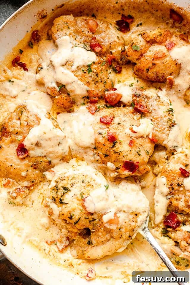 Top view of cooked cream sauce chicken thighs in a white skillet with a silver serving spoon picking up the food