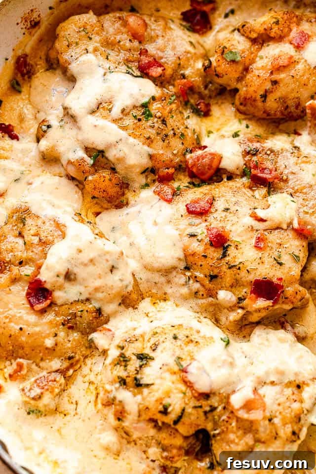 Top view shot of chicken thighs covered in cheese sauce and topped with diced bacon