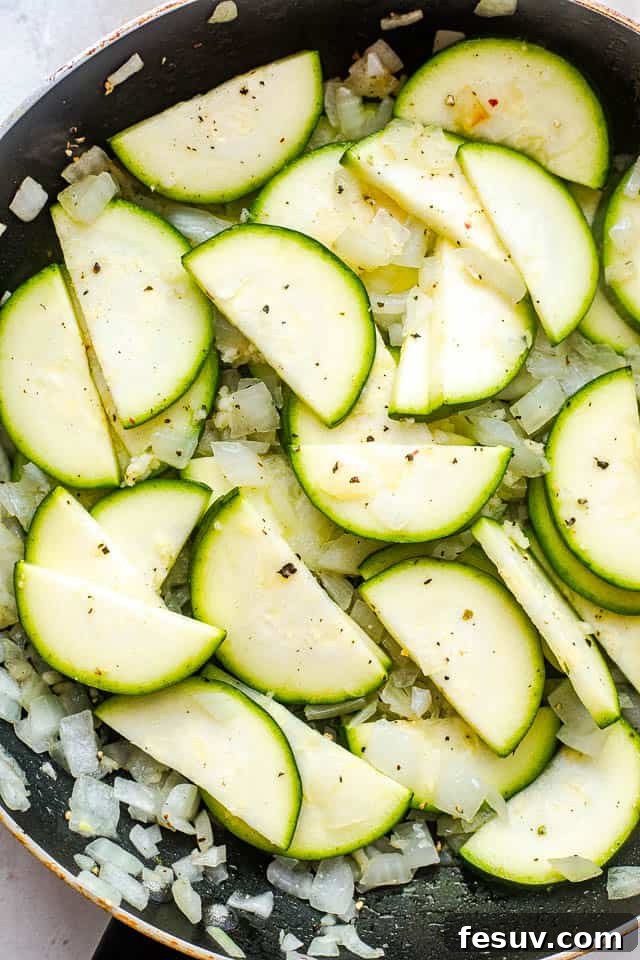 Velvety Zucchini Mushroom Pasta Bake 3 frying zucchini slices and diced onion in a black skillet