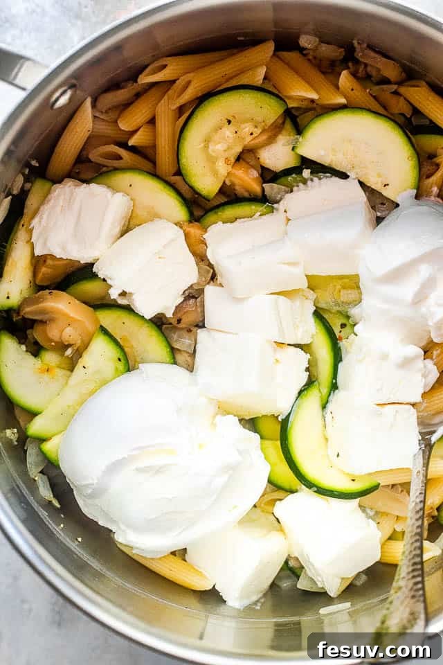Velvety Zucchini Mushroom Pasta Bake 4 overhead shot of a silver pot filled with pasta, zucchini slices, and cubed cream cheese