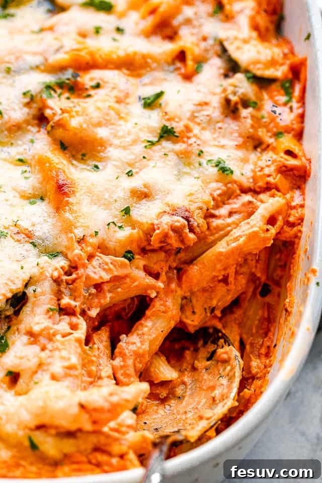 Velvety Zucchini Mushroom Pasta Bake 5 side view of a cheesy pasta in a baking dish with a serving spoon pulling out the food