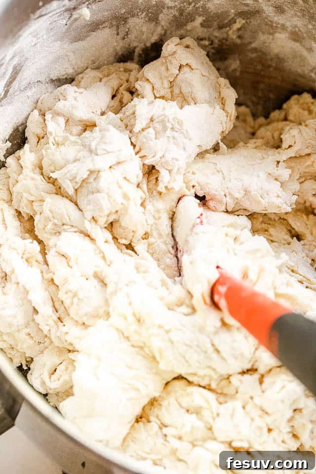 Effortless Artisan Bread 4 mixing bread dough with a red rubber spatula in a large clear bowl