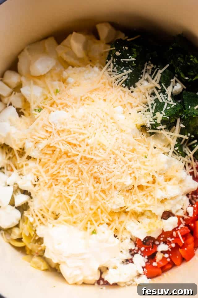 This Slow Cooker Spinach Artichoke Dip is a festive and delicious dip featuring artichokes, sweet red peppers and a medley of cheeses. Overhead shot of all ingredients for slow cooker spinach artichoke dip layered in a slow cooker before cooking.