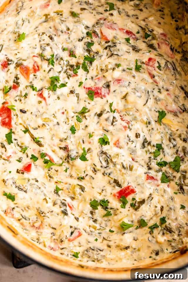 This Slow Cooker Spinach Artichoke Dip is a festive and delicious dip featuring artichokes, sweet red peppers and a medley of cheeses. Close-up overhead shot of bubbling, creamy spinach artichoke dip after cooking, ready to be served.