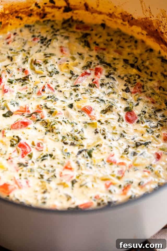 This Slow Cooker Spinach Artichoke Dip is a festive and delicious dip featuring artichokes, sweet red peppers and a medley of cheeses. A slow cooker filled with warm, bubbling spinach artichoke dip, garnished with fresh herbs, ready for serving.