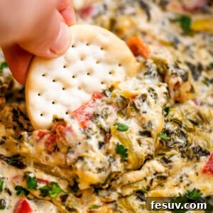 Effortless Slow Cooker Spinach Artichoke Dip 2 dipping a round cracker in spinach artichoke dip