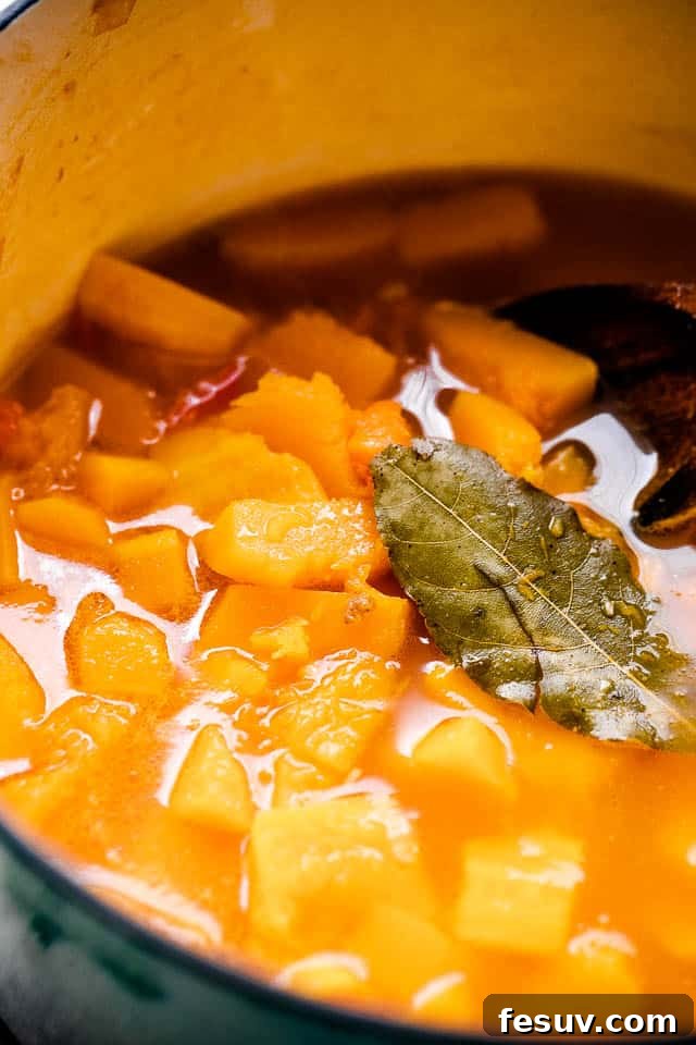 Diced Butternut squash simmering in broth, with a bay leaf set on top of the liquid.