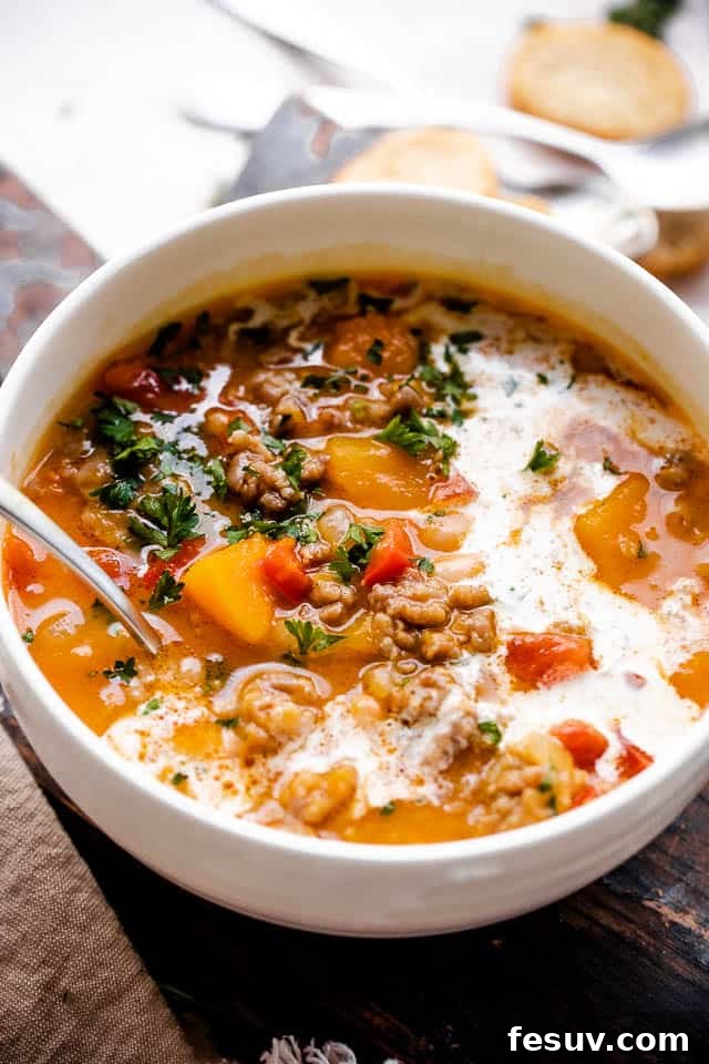 Side shot of butternut squash and sausage soup with cream in a white soup bowl.