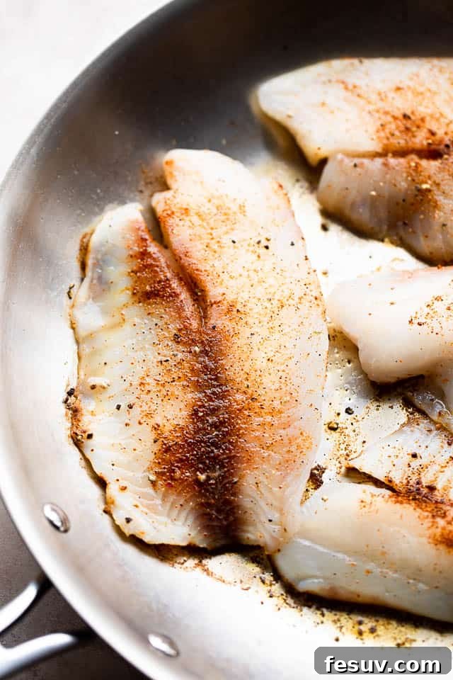 Close-up shot of tilapia fillets searing in a hot skillet, showing a golden-brown crust forming on the fish.